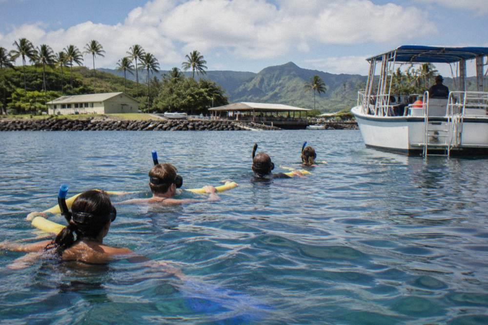Snorkelers holding a float line in open ocean with a boat nearby