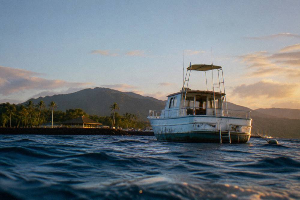 Small boat anchored in deep blue open water far from the Oahu coastline