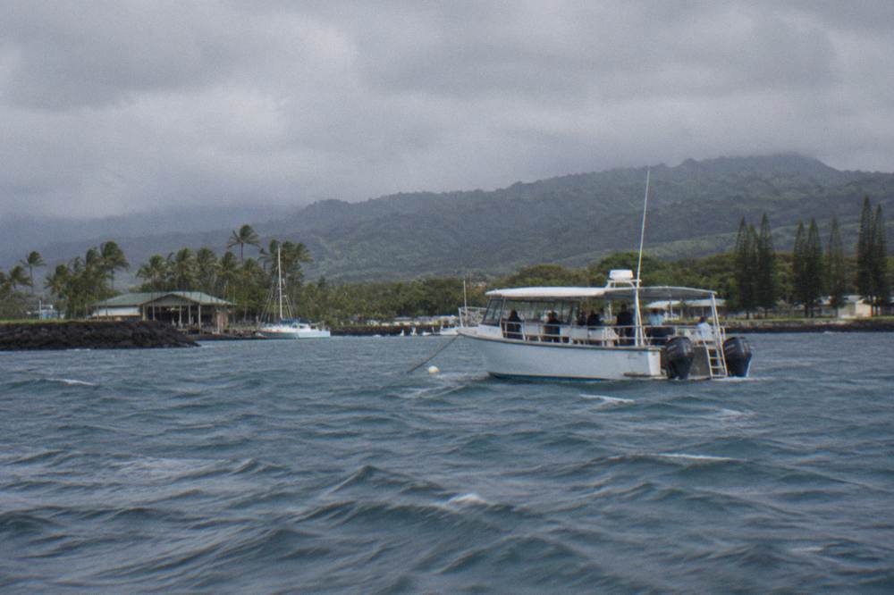 A shark tour boat anchored in calm blue open water with the Oahu coastline in the distance