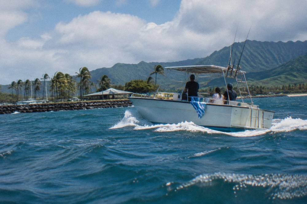 A small charter boat crossing open blue water offshore of Oahu