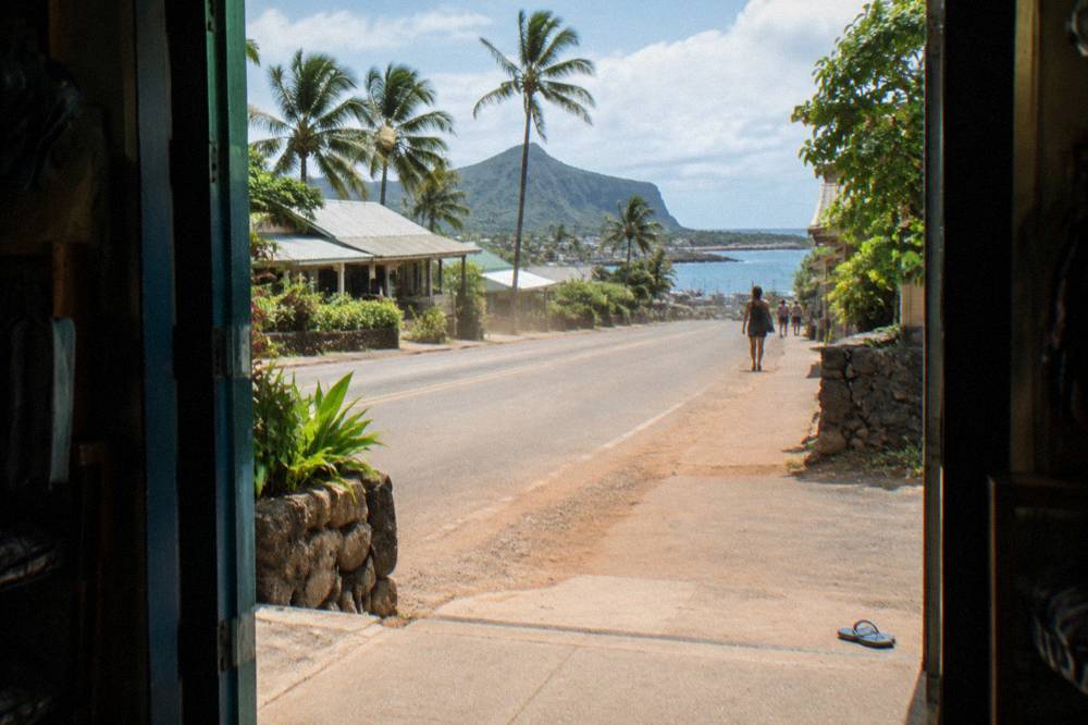 Coastal highway road leading toward a small harbor town with palm trees