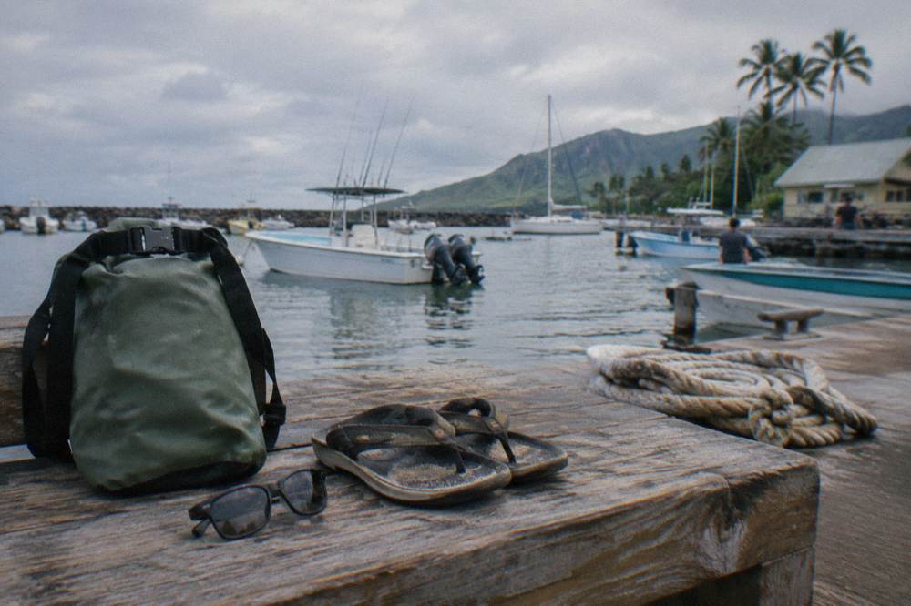 Dry bag, sunglasses and sandals arranged on a dock bench beside a boat